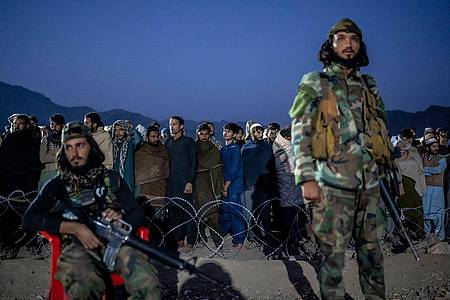Taliban-Kämpfer stehen Wache, während afghanische Flüchtlinge in einem Lager nahe der pakistanisch-afghanischen Grenze anstehen, um sich registrieren zu lassen.