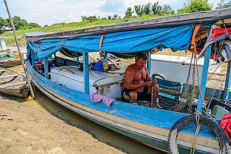 Ein Fischer sitzt fast im Trockenen in seinem Boot und flickt ein Netz. Die Dürre bereitet den Flussbewohnern nicht nur Schwierigkeiten beim Fischen, sondern auch beim Verkehr. Dörfer sind in der Region über die Flüsse vernetzt.