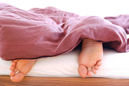 nackte Füße schauen am Bettende unter einer Decke hervor