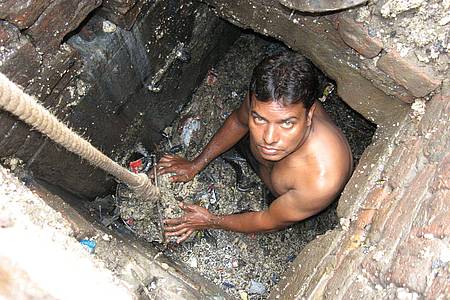 Ein Kanalreiniger arbeitet in einem Außenbezirk von Neu Delhi in der Kanalisation - ohne Schutzkleidung.